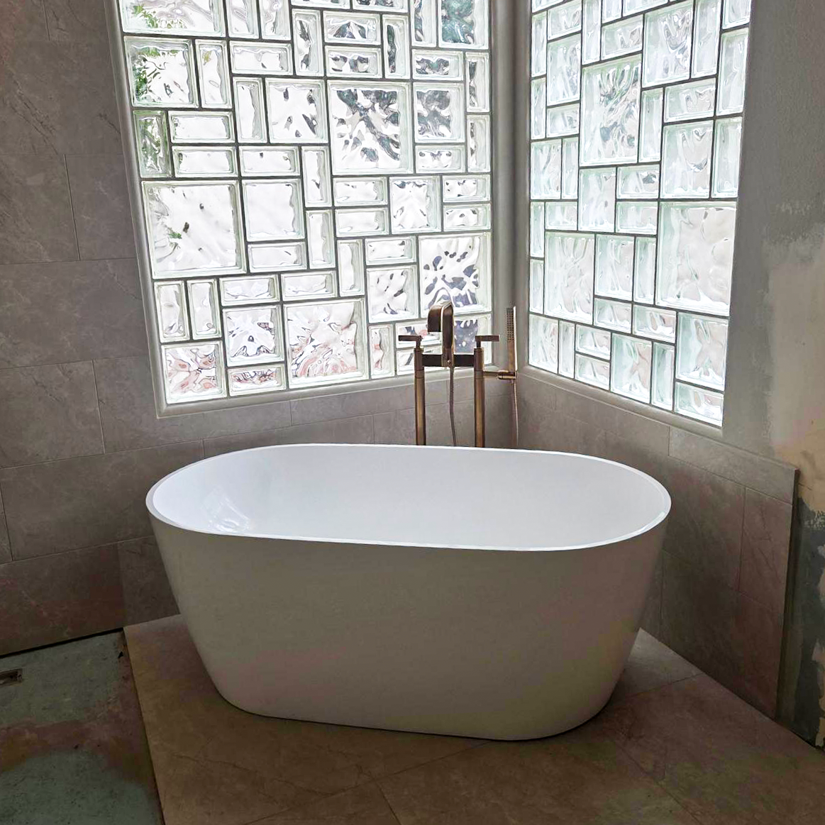 Freestanding soaking tub with gold fixtures and glass block window wall