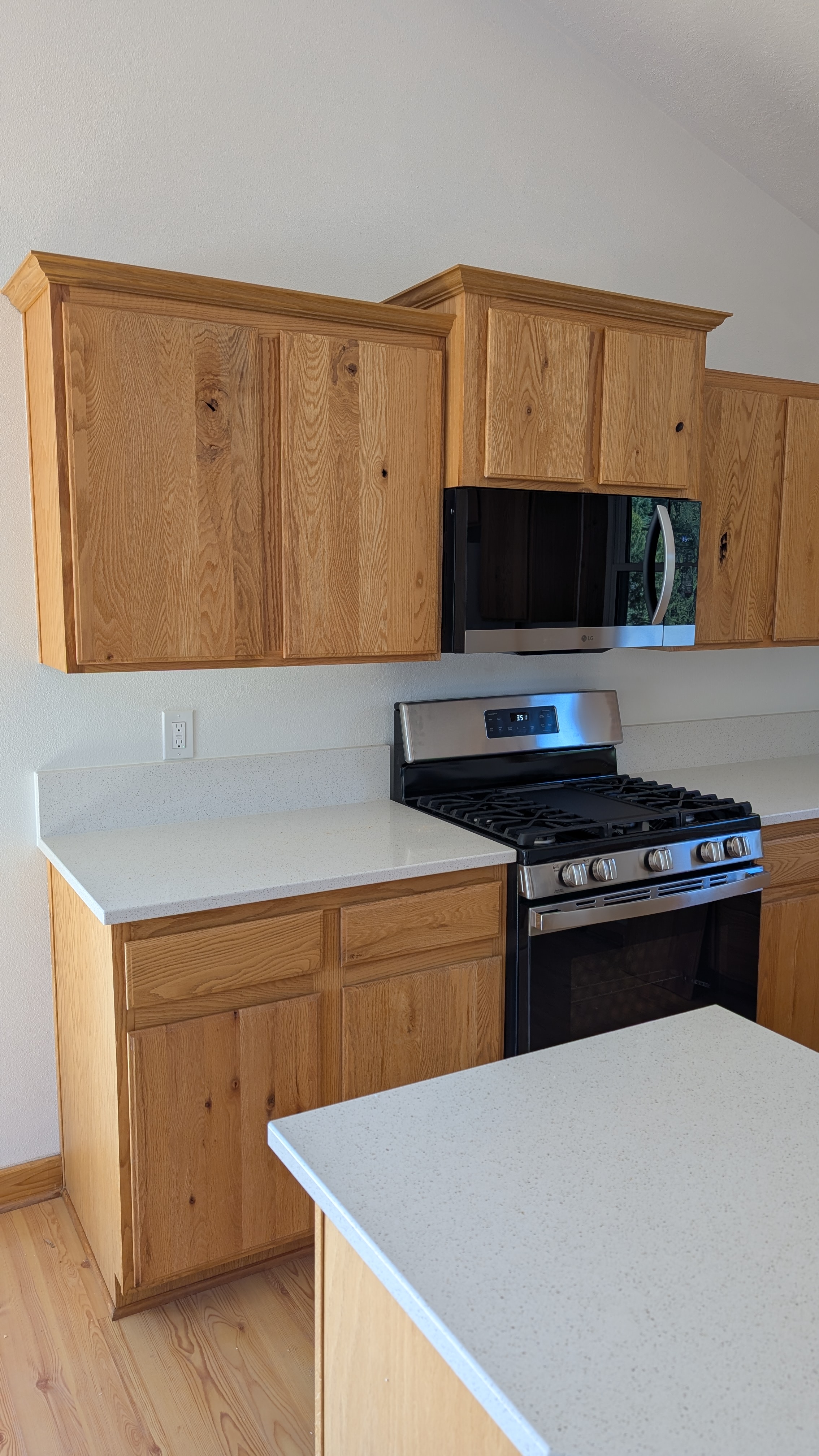 Natural oak kitchen cabinets with white quartz countertops and stainless appliances