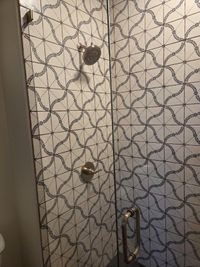 Close-up of patterned shower tile with a brass shower head and valve behind frameless glass