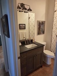 New walnut-tone vanity with a black countertop and brass faucet in a remodeled guest bathroom