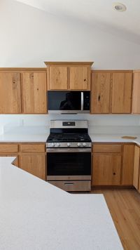 Oak kitchen with gas range and quartz countertops — finished installation