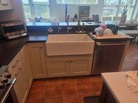 White farmhouse sink set into shaker base cabinets with black countertops and a stainless dishwasher